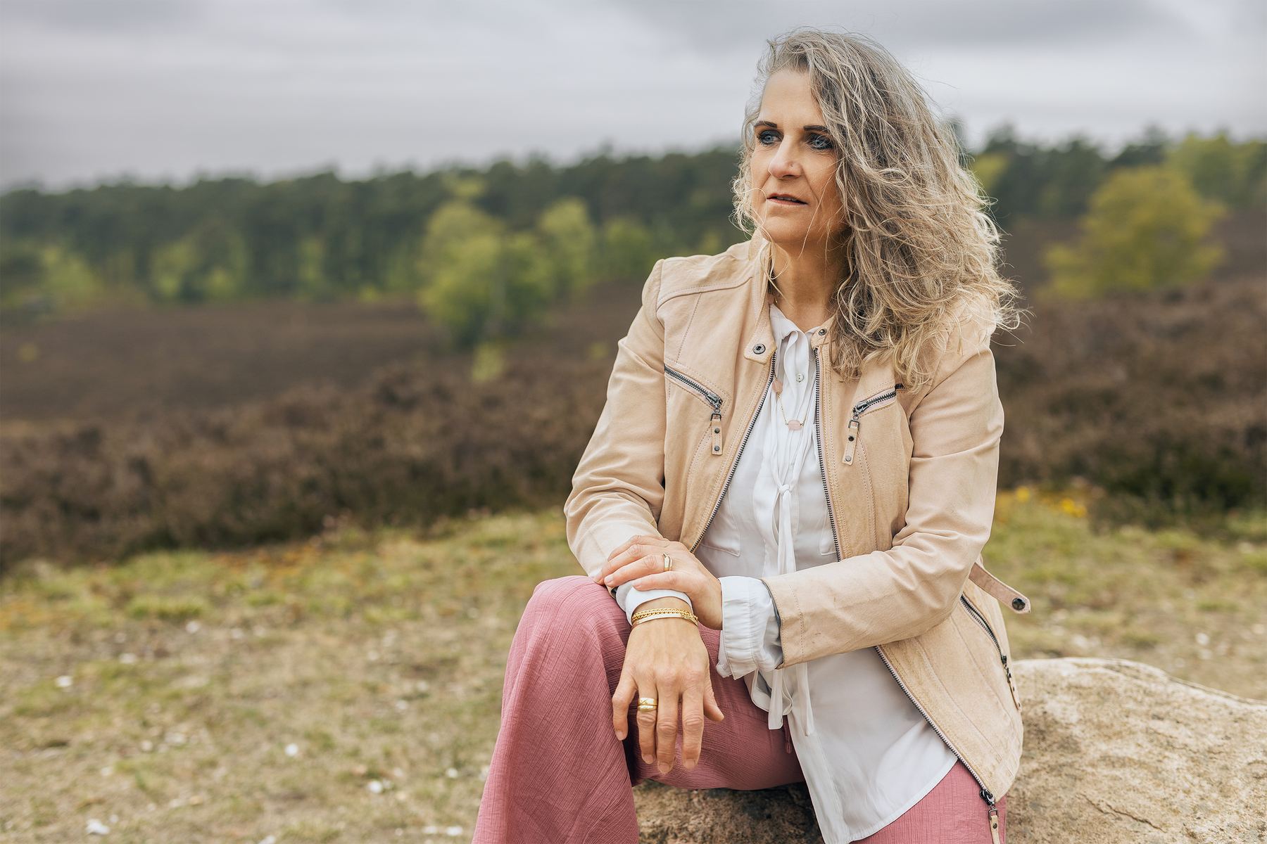Britta Selina sitzt auf einem Stein in der Heide und blickt in die Weite